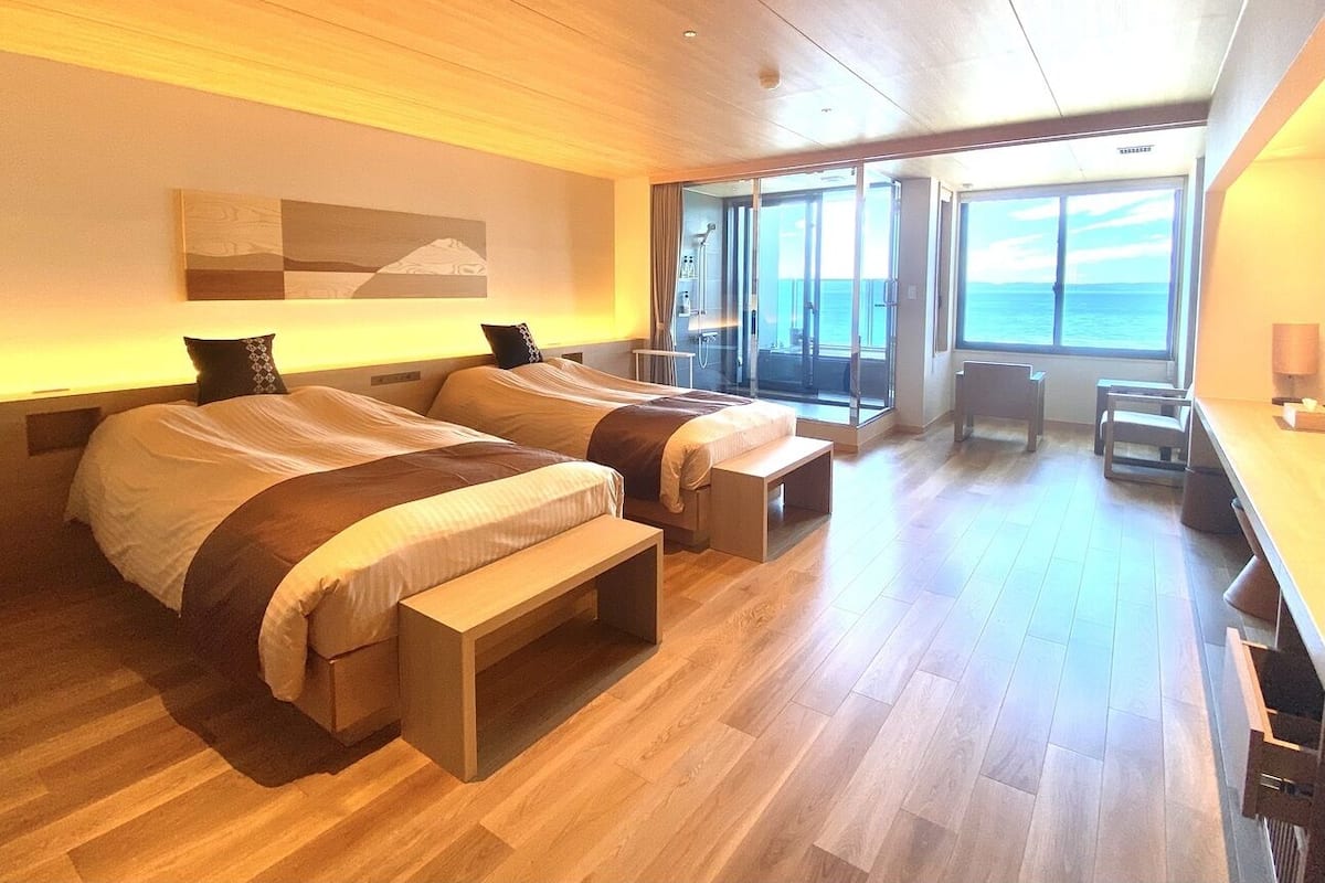 Ein modernes Hotelzimmer mit zwei Betten, einem großen Fenster und einem Balkon mit Meerblick.