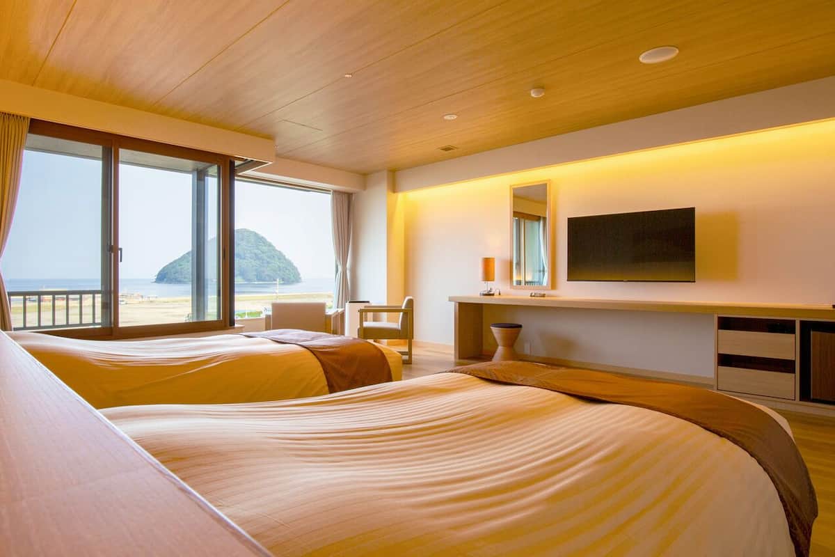 Ein Hotelzimmer mit einem großen Bett, einem Schreibtisch, einem Stuhl, einem Fernseher und Meerblick.
