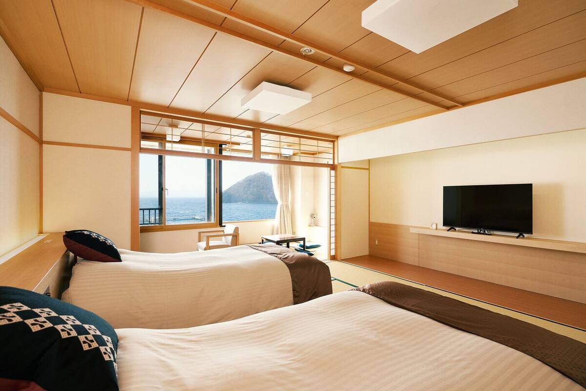 Ein Hotelzimmer mit zwei Betten, einem Fernseher, einem Fenster mit Meerblick und einem traditionellen japanischen Raumteiler.
