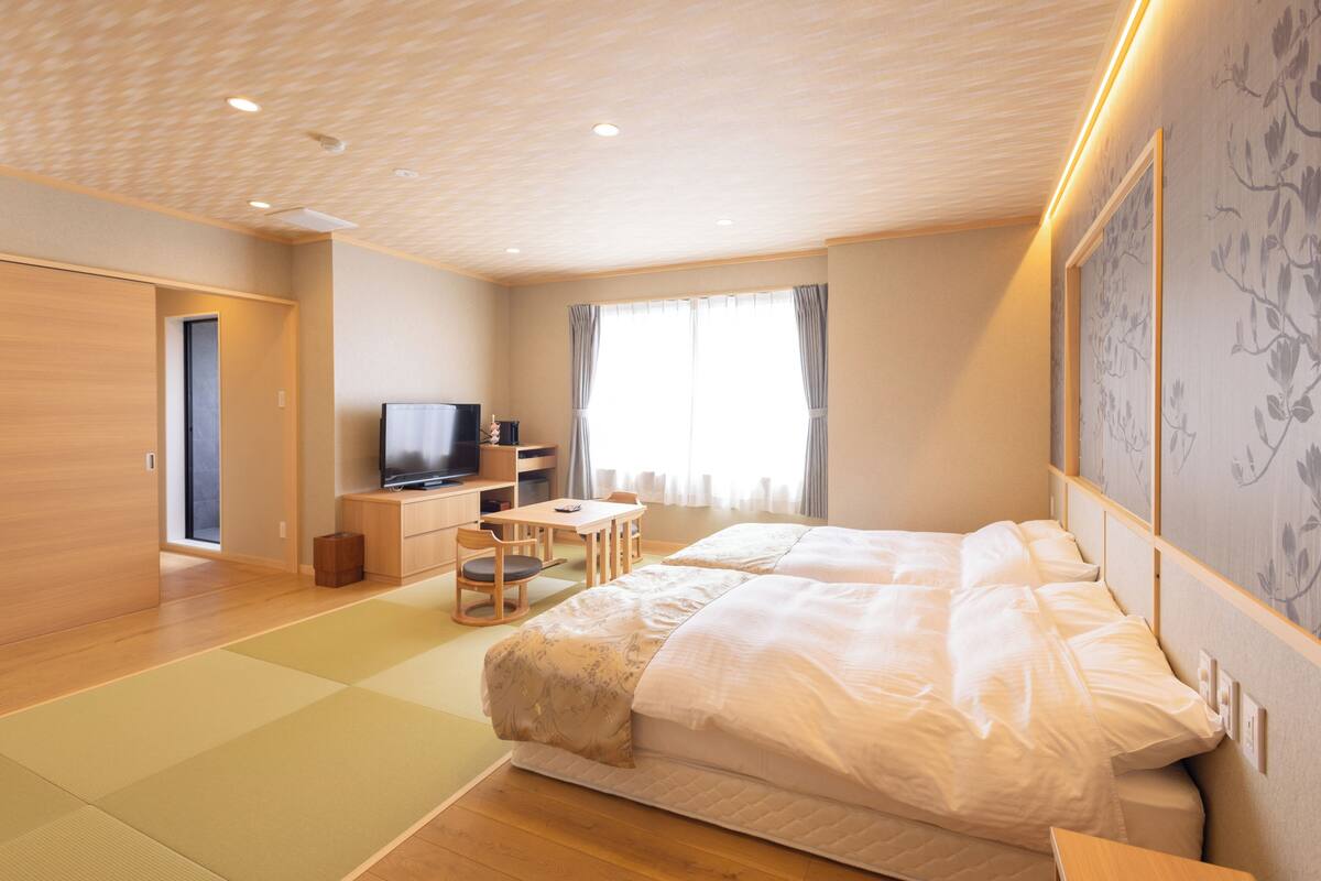A hotel room with a large bed, a TV, a desk, and a chair.