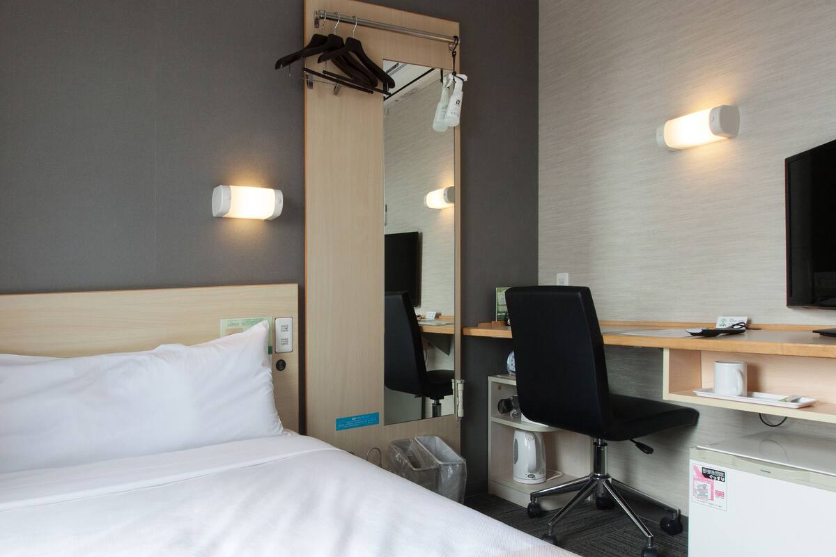 Une chambre d’hôtel équipée d’un lit, d’un bureau, d’une chaise, d’une télévision et d’un miroir.