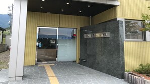 L’entrée du Super Hôtel se distingue par sa façade recouverte de carreaux, sa porte en verre transparent et son panneau indicateur.