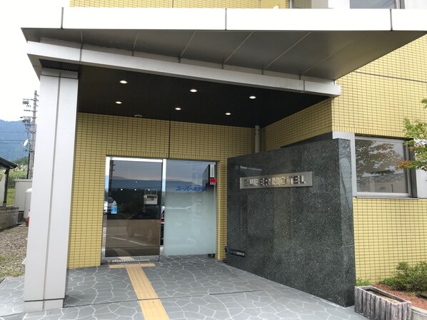 La entrada del Super Hotel, con fachada de azulejos, puerta de cristal transparente y una señal.