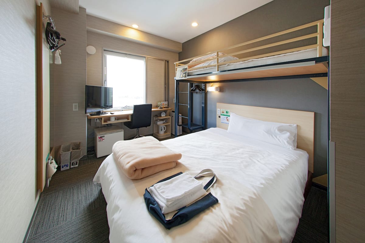 Une chambre d’hôtel avec un lit superposé, un bureau avec un ordinateur, une chaise et un téléviseur.