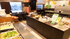 Un espace buffet proposant différents stands de nourriture, notamment des plateaux de fruits de mer, des salades et d’autres plats. Des tables et des chaises sont à disposition pour les repas, ainsi qu’un comptoir où est affiché le menu.