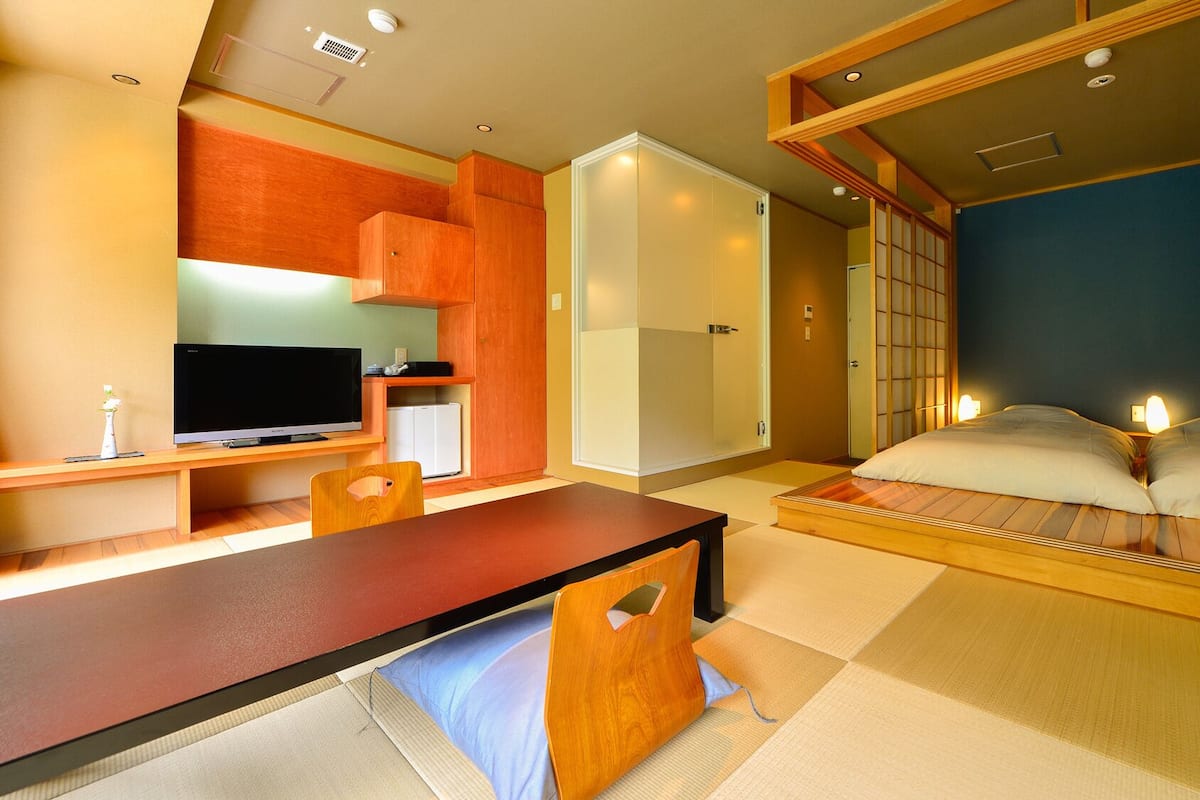 Une pièce traditionnelle japonaise avec un sol recouvert de tatamis, une table basse, un lit avec un futon et des portes coulissantes.