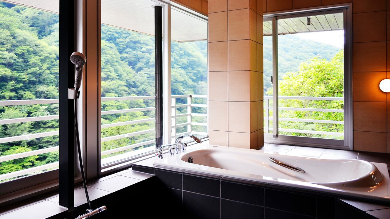 A bathroom with a bathtub, a shower, and a window with a view of a forested area.