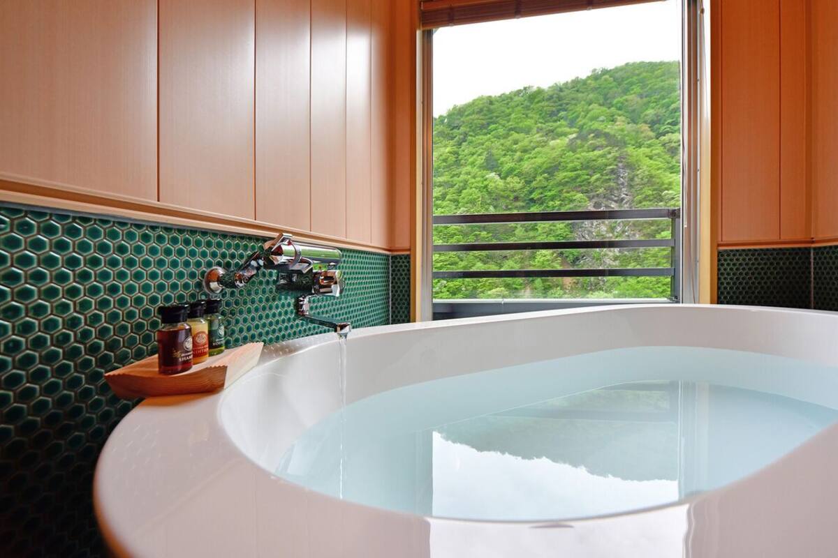 Une salle de bain avec une baignoire, une étagère en bois où sont rangés les articles de toilette, et une vue sur une forêt verdoyante par la fenêtre.