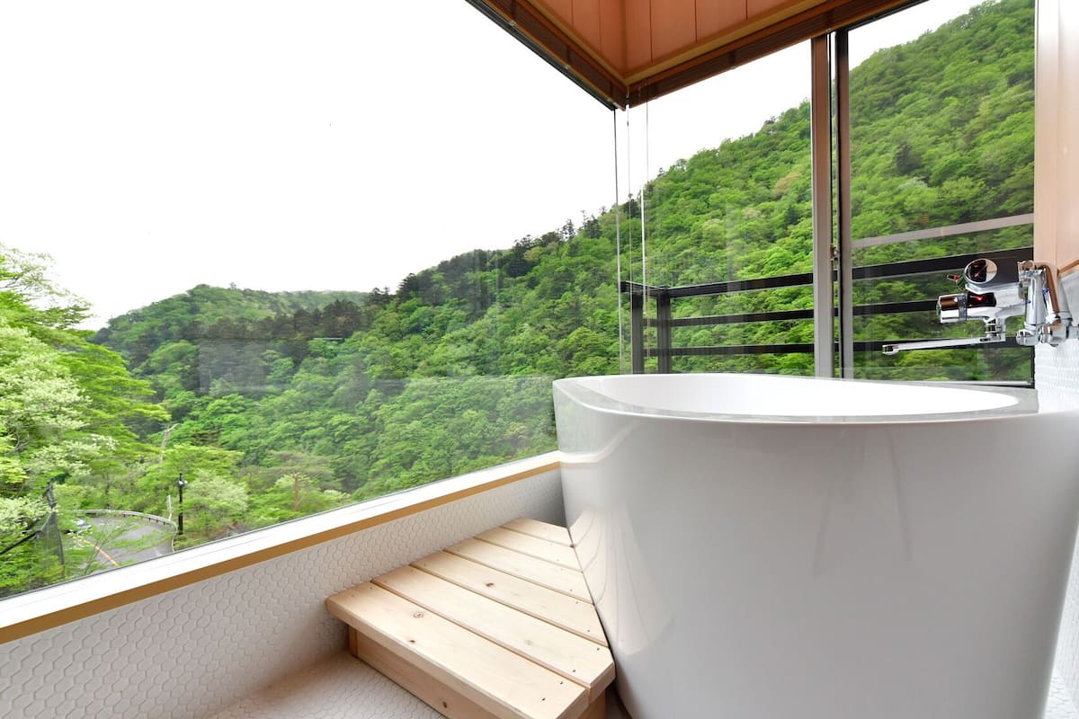 Une salle de bain dotée d’une grande baignoire, d’un escalier en bois et offrant une vue sur une colline boisée.