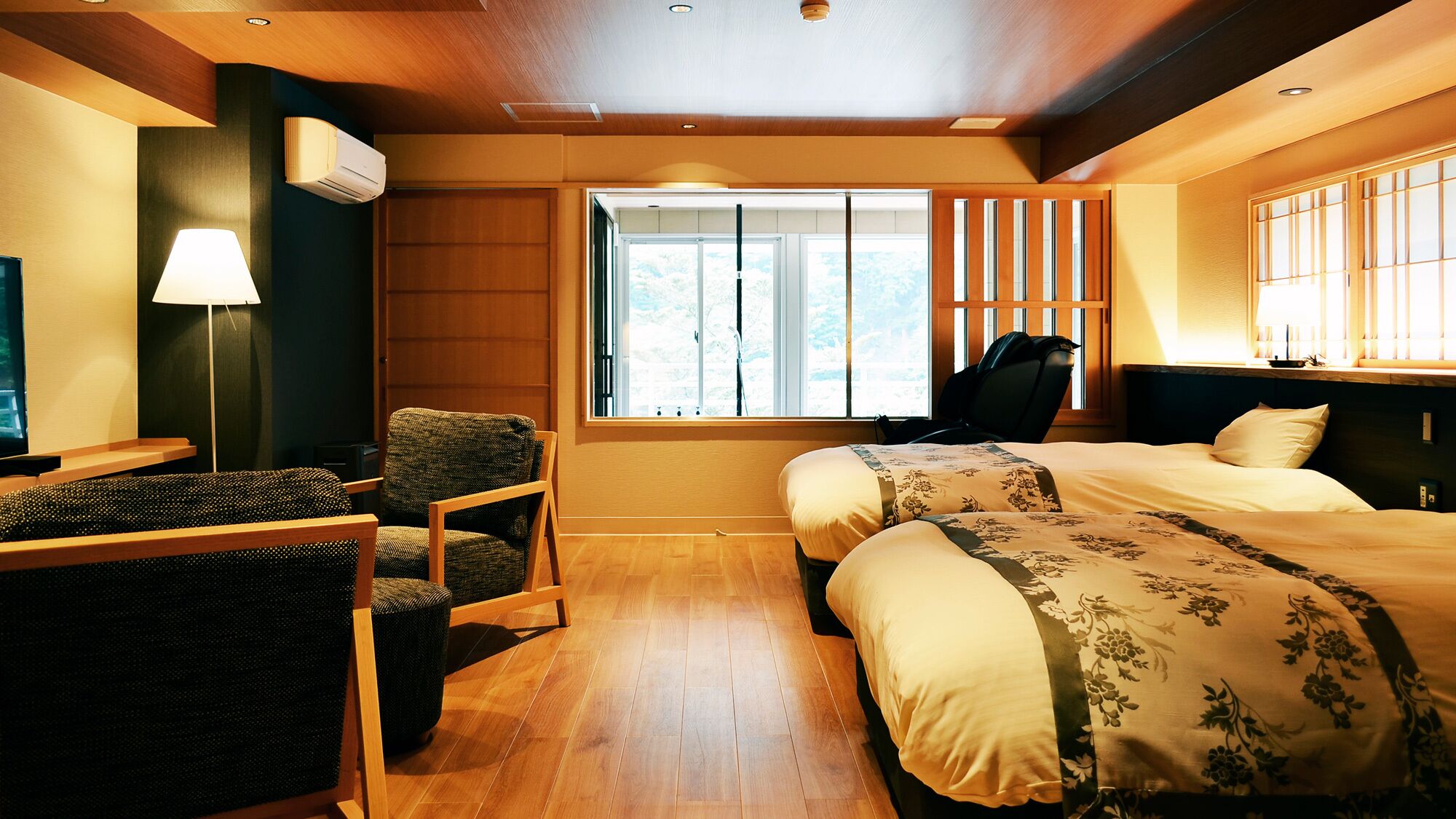Une chambre d’hôtel avec deux lits, un bureau avec une chaise, une lampe et une fenêtre avec des stores.
