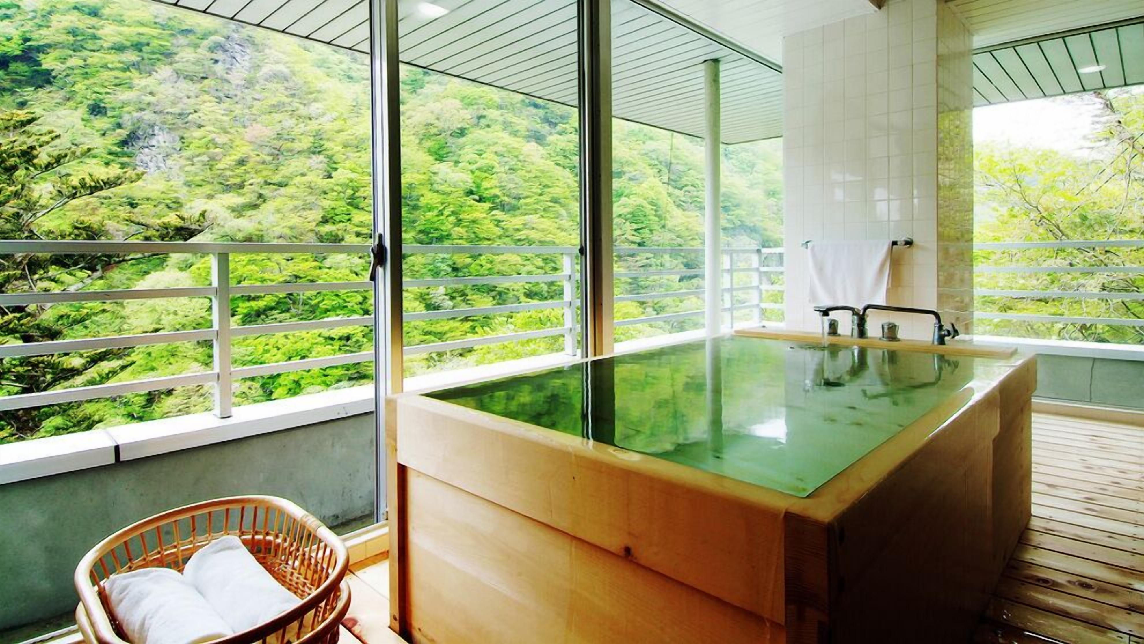 Une salle de bain moderne dotée d’un jacuzzi entouré de parois en verre, d’un plancher en bois et offrant une vue sur une forêt luxuriante.