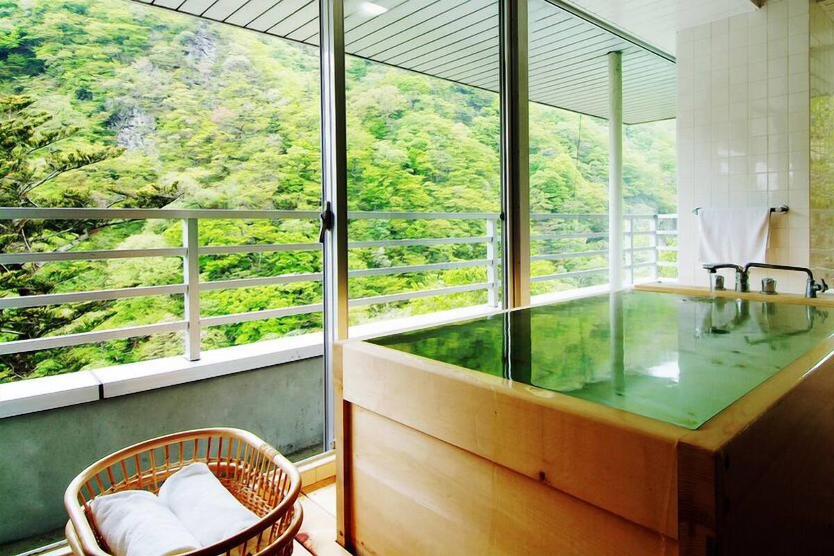 Une salle de bain moderne dotée d’un jacuzzi entouré de parois en verre, d’un plancher en bois et offrant une vue sur une forêt luxuriante.