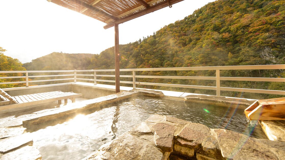 A hot spring bath area with stone steps, wooden benches, and a wooden pergola.
