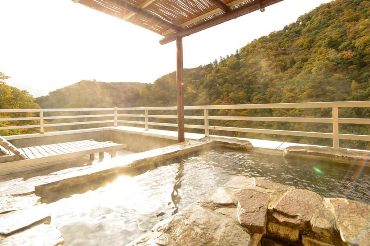 Un espace de baignade dans une source thermale, avec des marches en pierre, des bancs en bois et une pergola en bois.