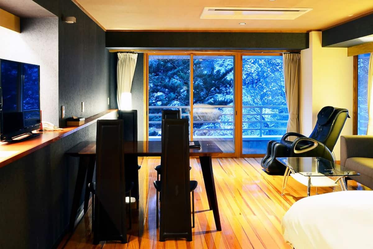 Une chambre d’hôtel avec un lit, un bureau avec un ordinateur, une chaise, un canapé et une grande fenêtre donnant sur des arbres.