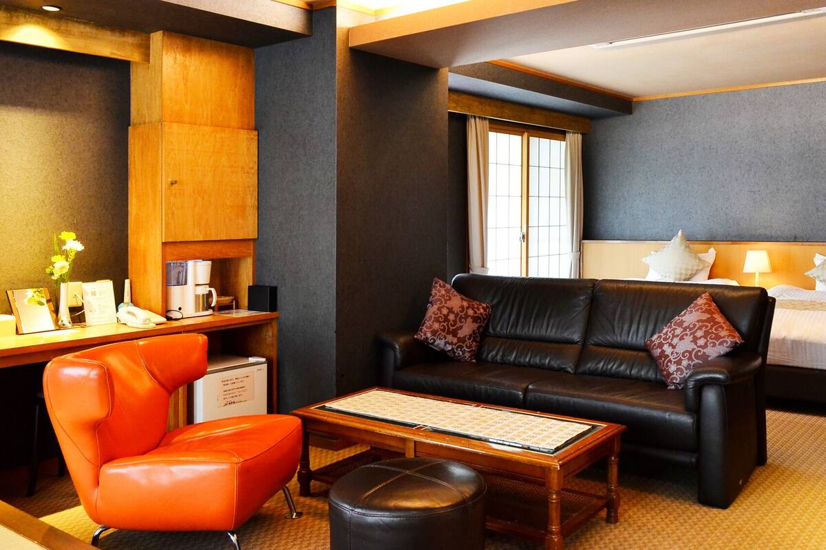 Une chambre d’hôtel avec un canapé en cuir, un bureau en bois, un lit et une fenêtre.