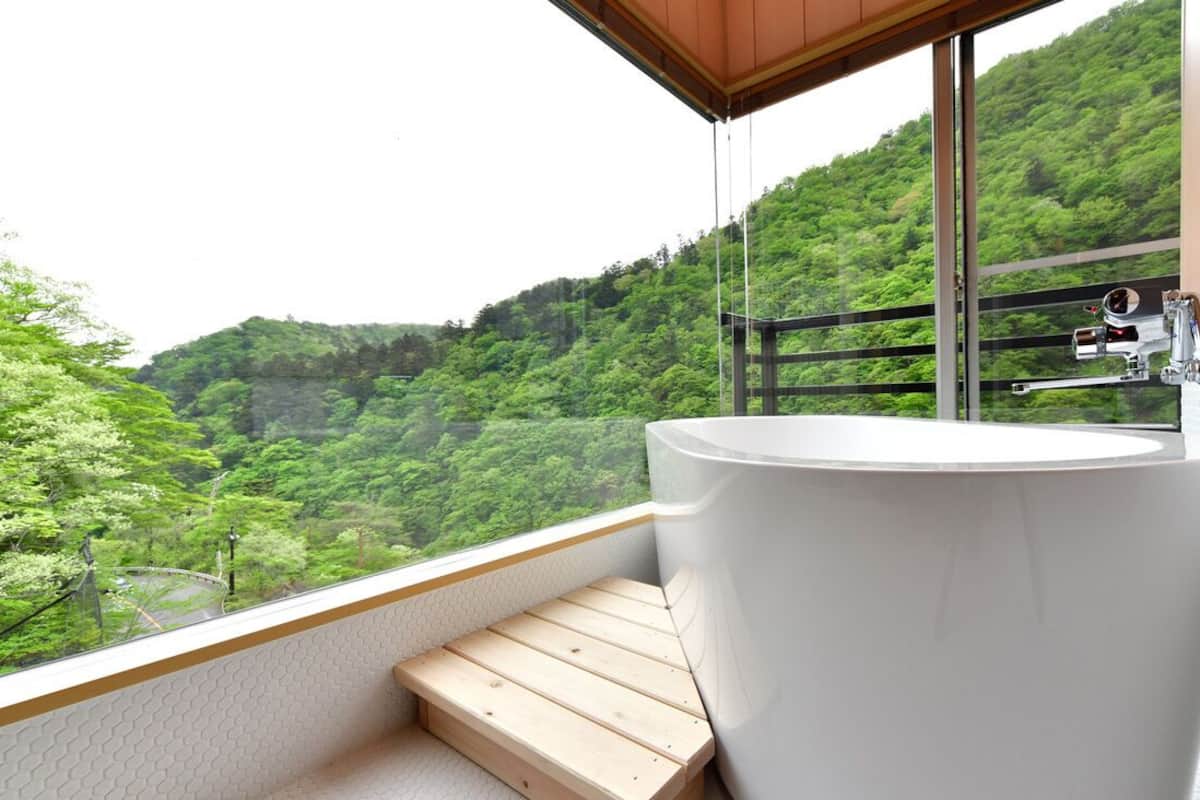 Une salle de bain dotée d’une grande baignoire, d’un banc en bois et offrant une vue sur une colline verdoyante.