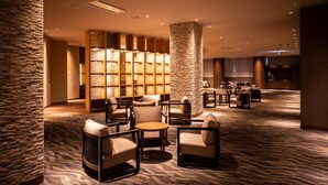 Un hall d’hôtel avec un mur en pierre, un espace détente avec des chaises et des tables, et un comptoir d’accueil.
