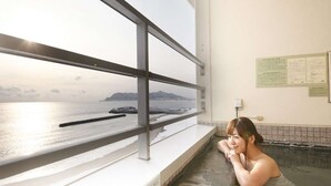 Une personne se détend dans une source thermale, avec vue sur la mer à travers une fenêtre.
