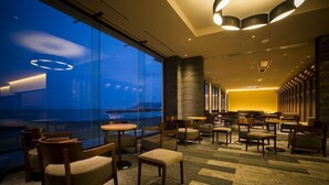 Un hall d’hôtel moderne avec un grand mur de verre donnant sur le paysage urbain au crépuscule.