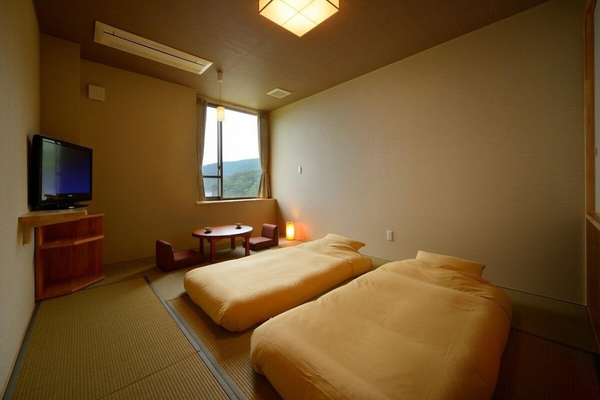 Habitación de hotel con dos camas, televisión, una mesita con sillas, ventana con vistas y luz en el techo.