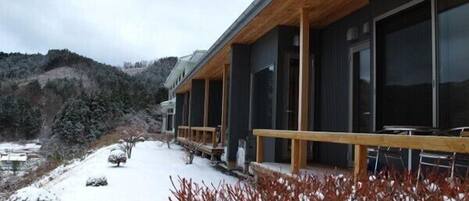 Un edificio moderno con terraza de madera y ventanas amplias, rodeado de un paisaje cubierto de nieve.