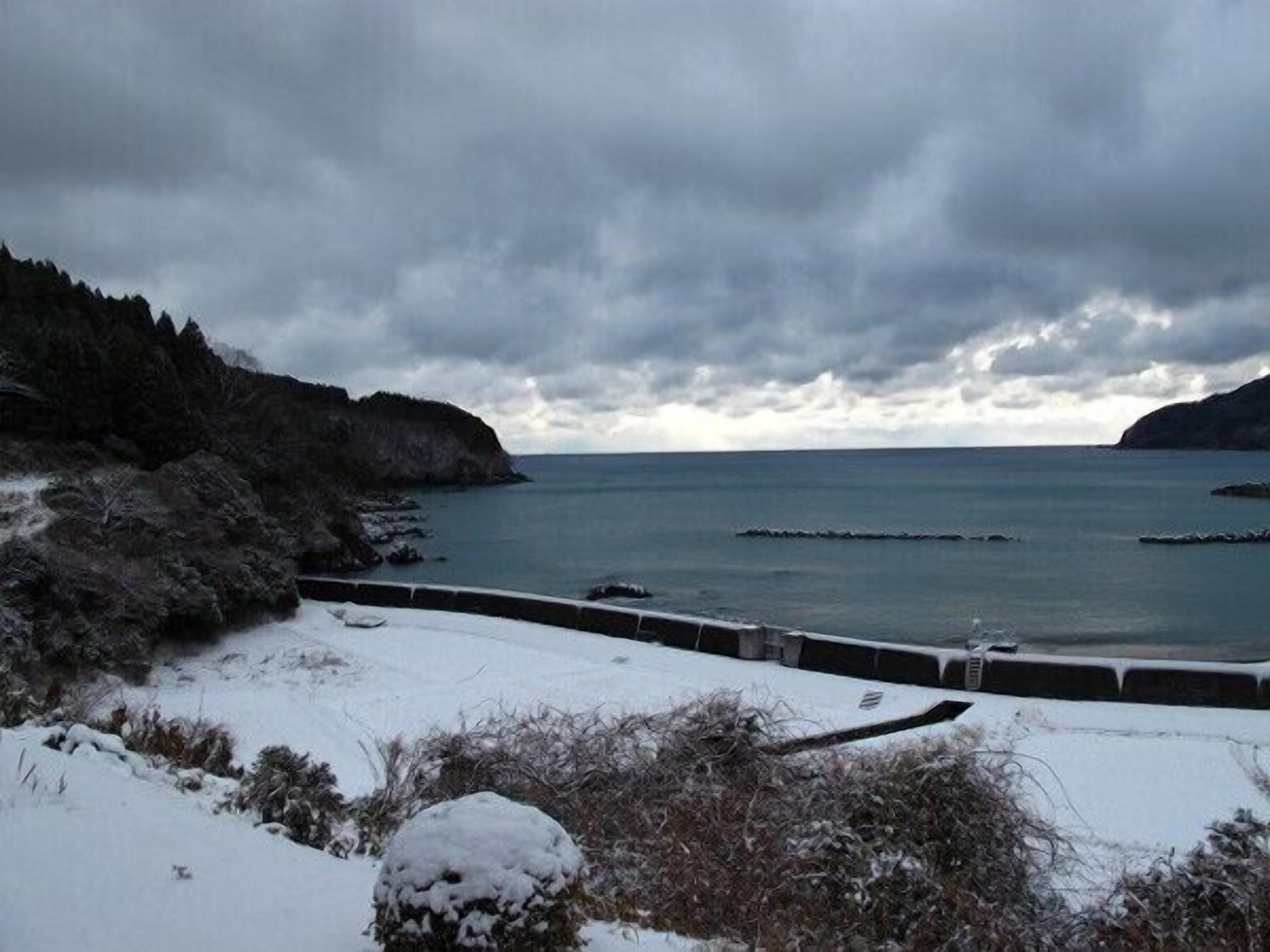 A coastal landscape with snow-covered ground and rocky cliffs.
