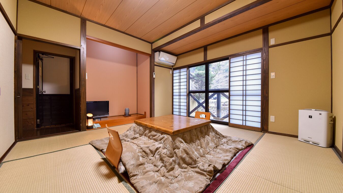 Ein traditioneller japanischer Raum mit Tatami-Böden, einem niedrigen Holztisch, einem Fernseher und einer Schiebetür mit Aussicht.