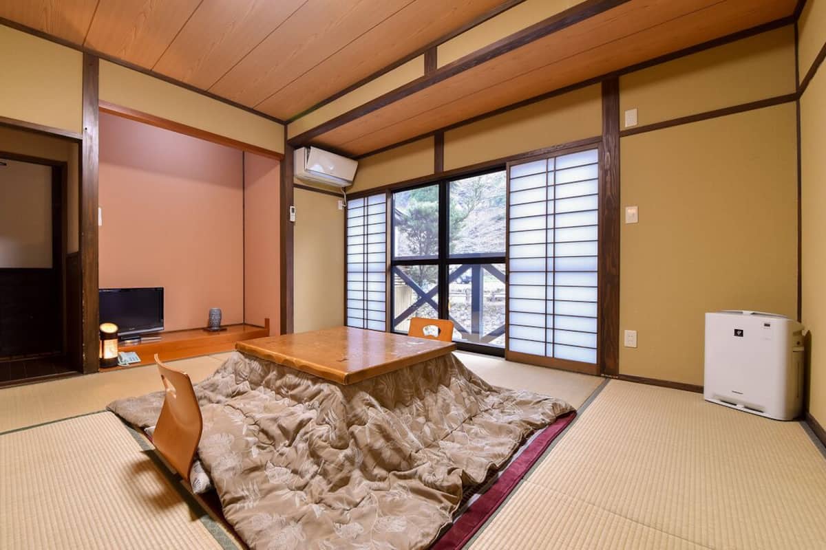 A traditional Japanese room with tatami flooring, a low wooden table, a television, and a sliding door with a view.