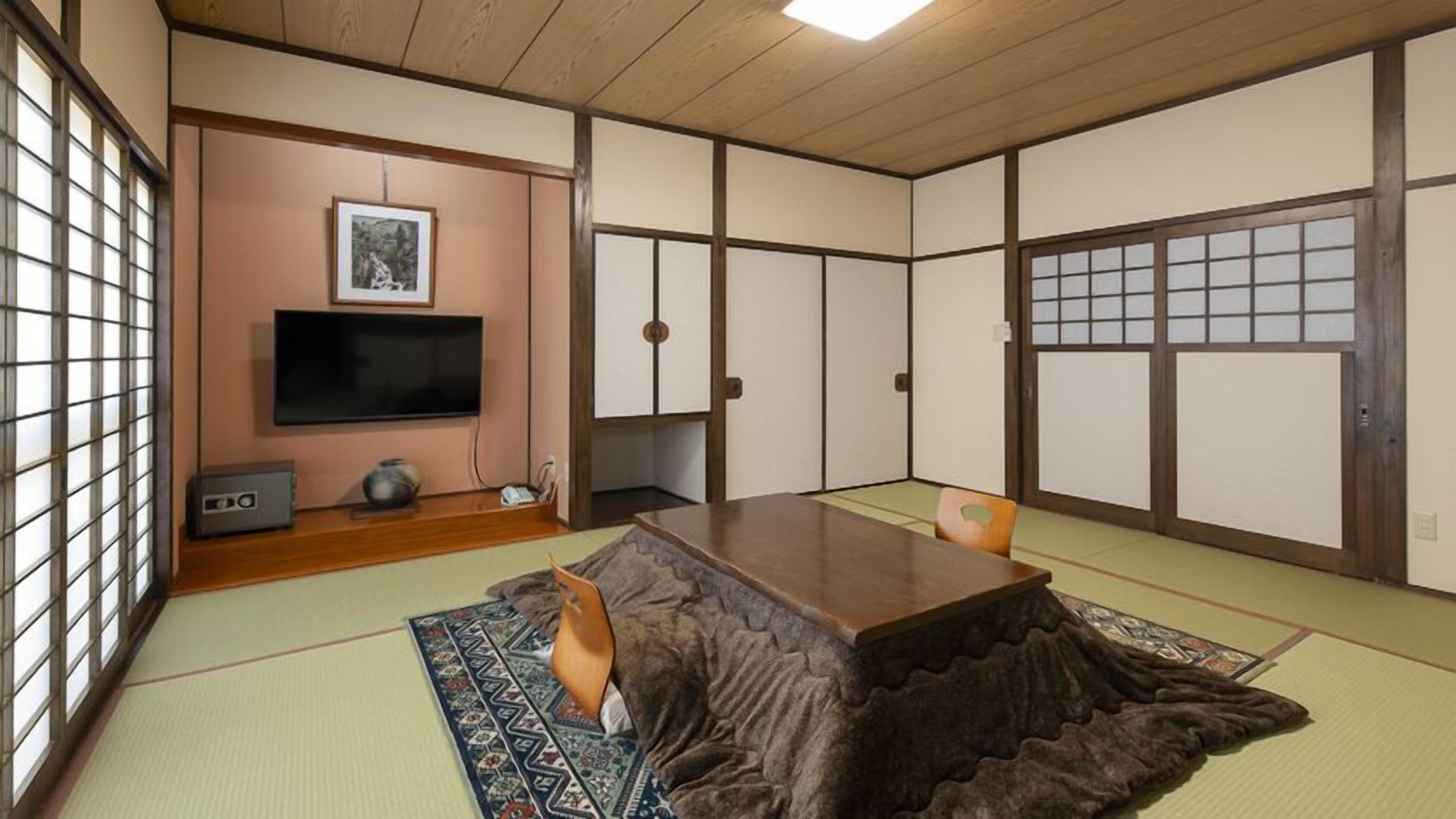 Ein Zimmer mit Tatami-Matten, einem Fernseher, einem Schrank und einer traditionellen japanischen Schiebetür.
