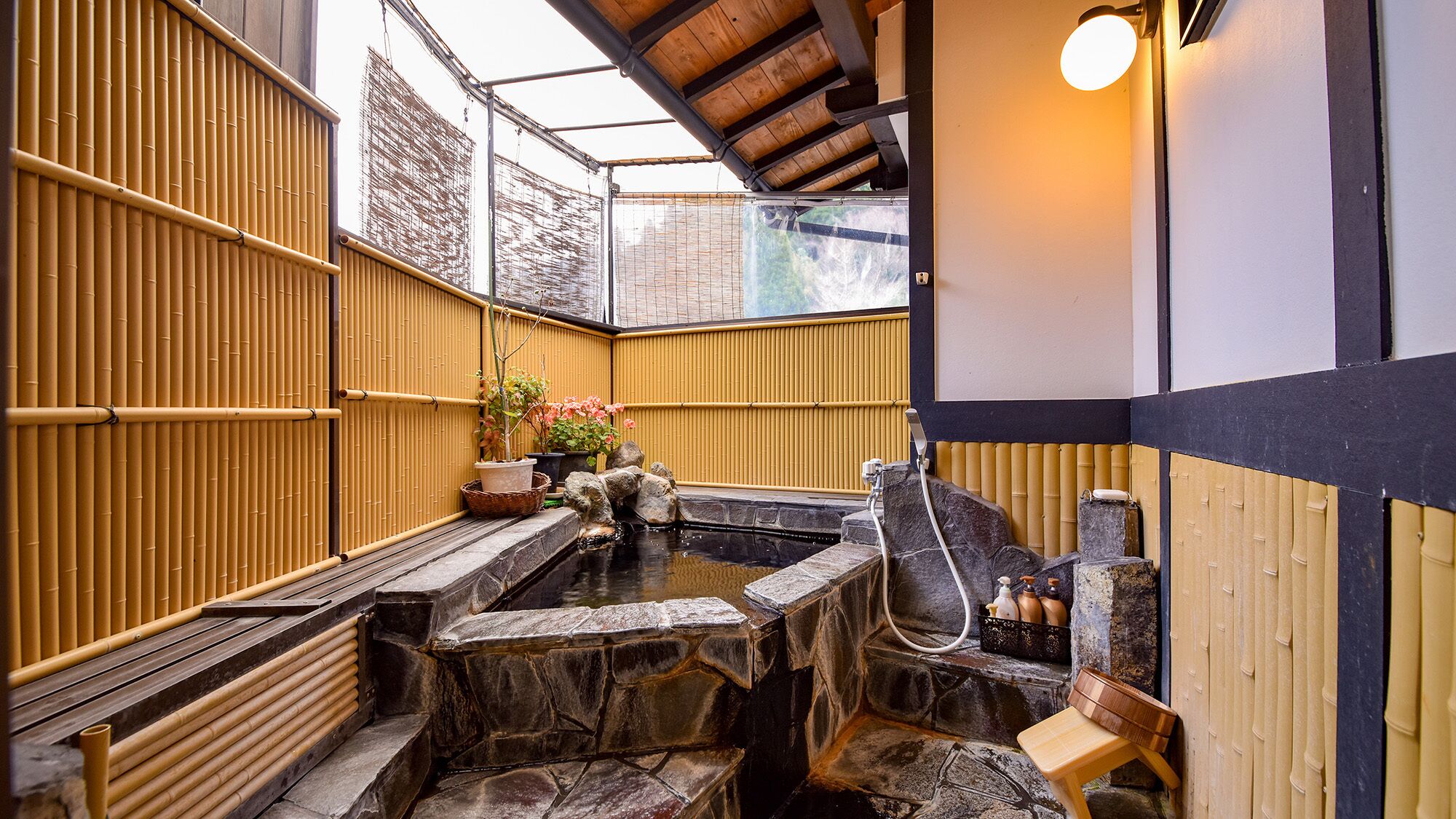 A traditional Japanese onsen with stone steps, bamboo walls, and a wooden bench.