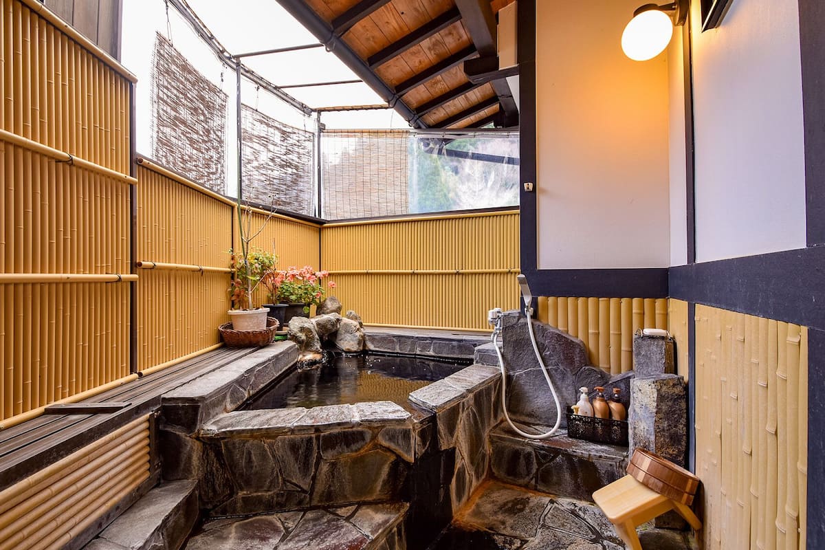 A traditional Japanese onsen with stone steps, bamboo walls, and a wooden bench.