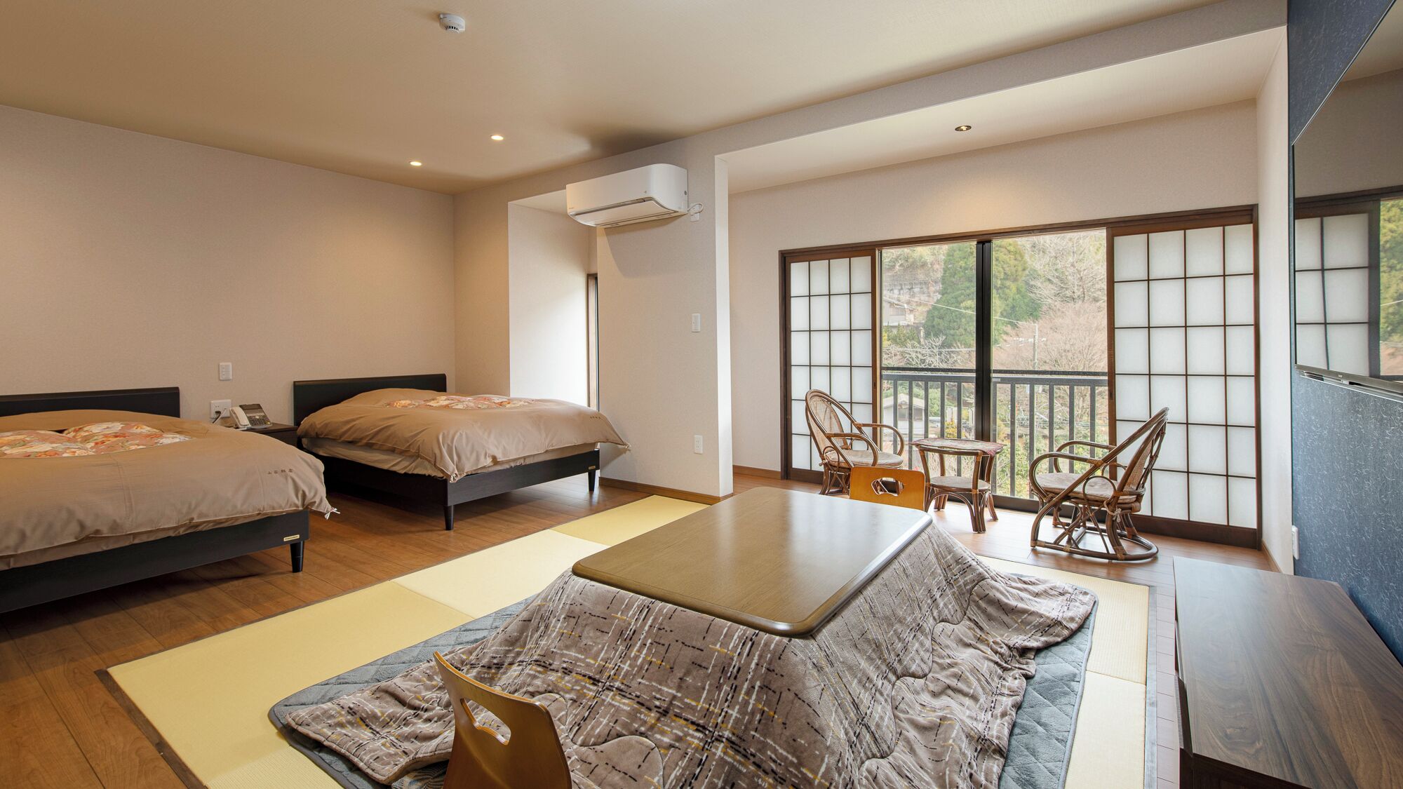 A hotel room with two beds, a dining table, chairs, a view through a large window, and an air conditioning unit.