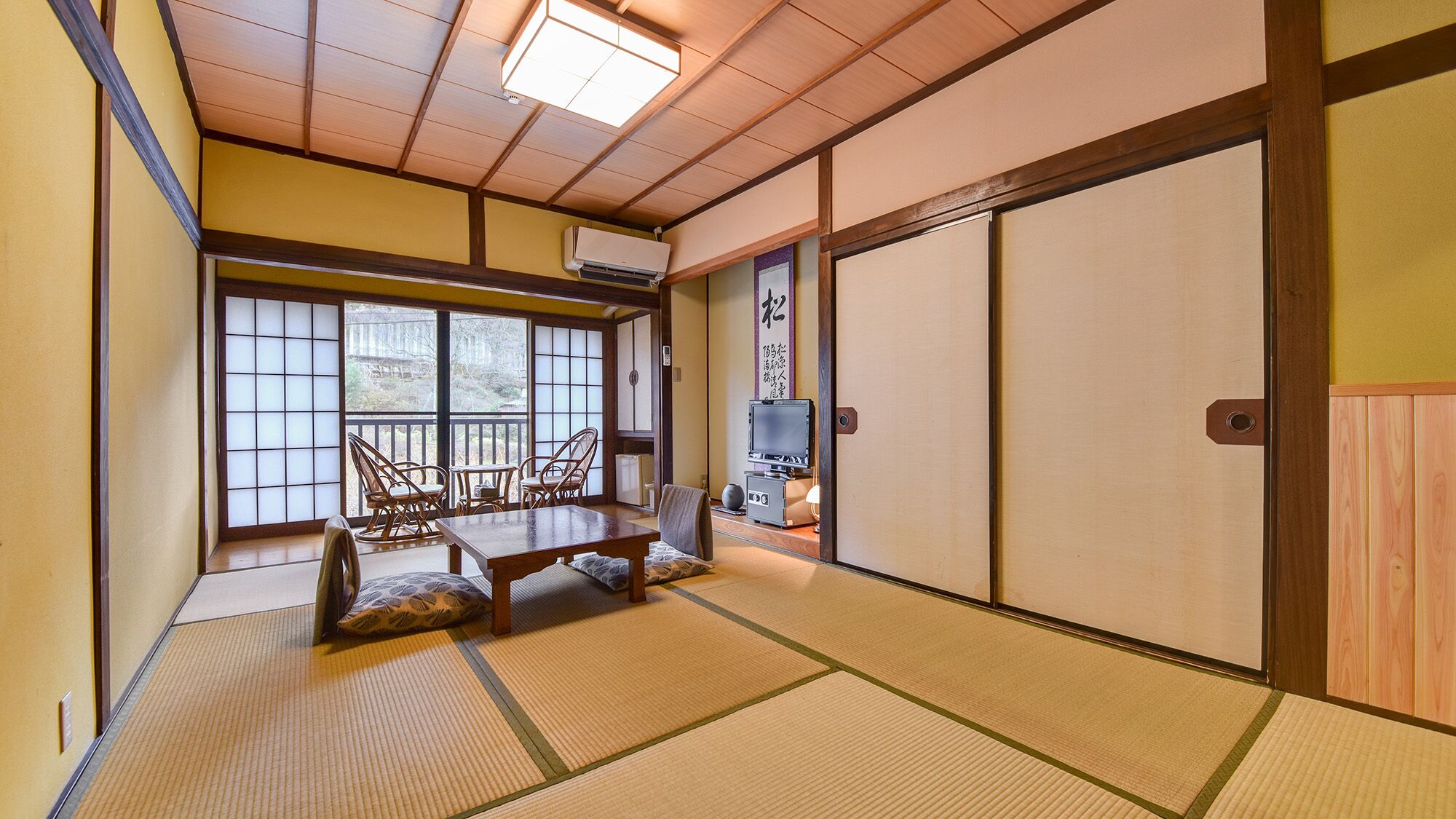 A traditional Japanese room with tatami flooring, a low table with cushions, and a television.