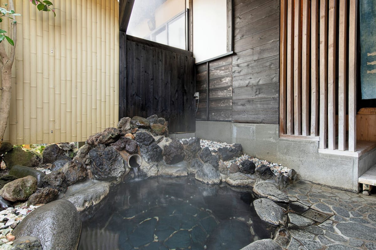 A traditional Japanese onsen with a stone hot spring, wooden benches, and a bamboo fence.