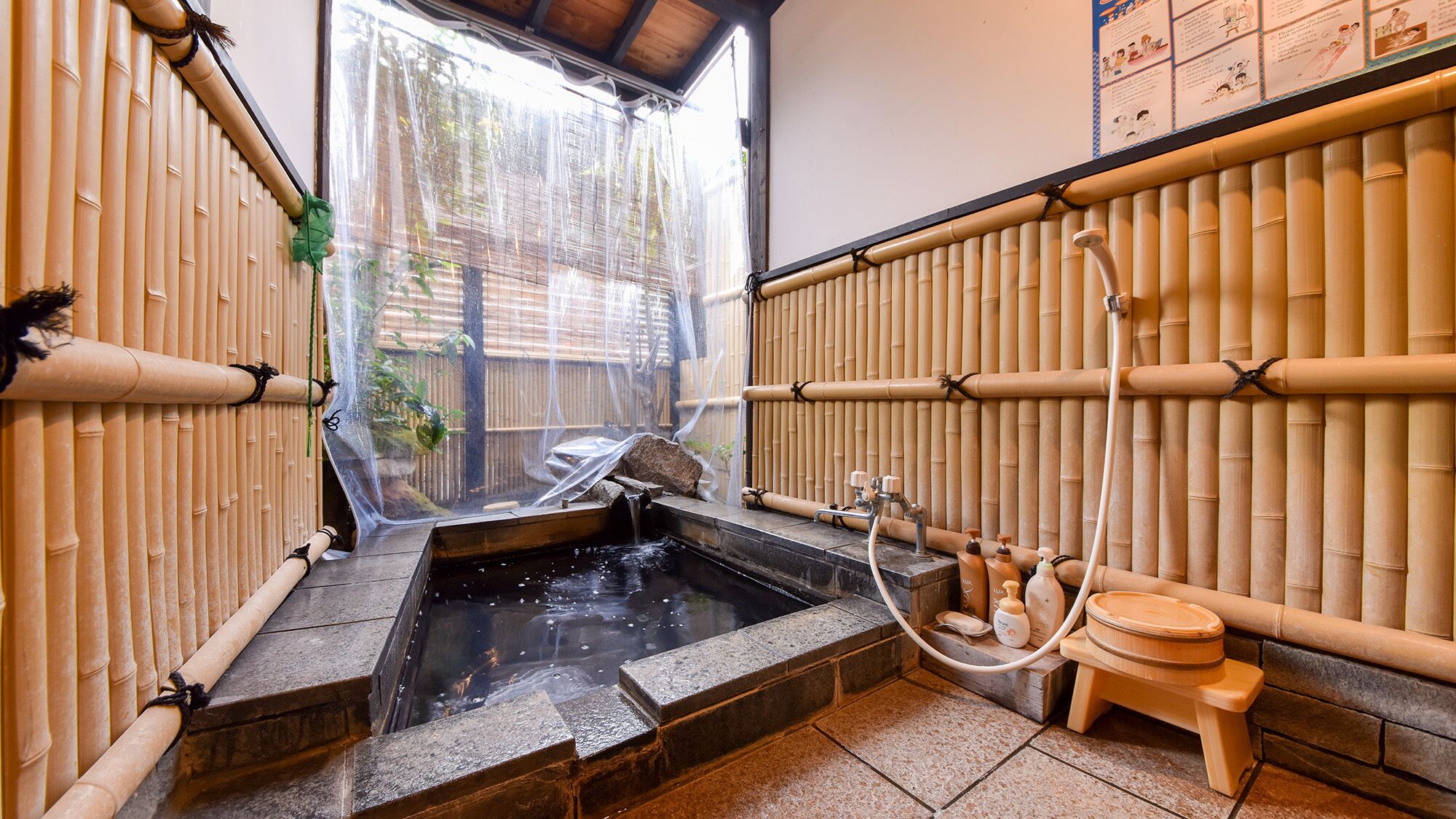 A traditional Japanese onsen with bamboo walls, a stone hot spring, and a wooden washbasin.