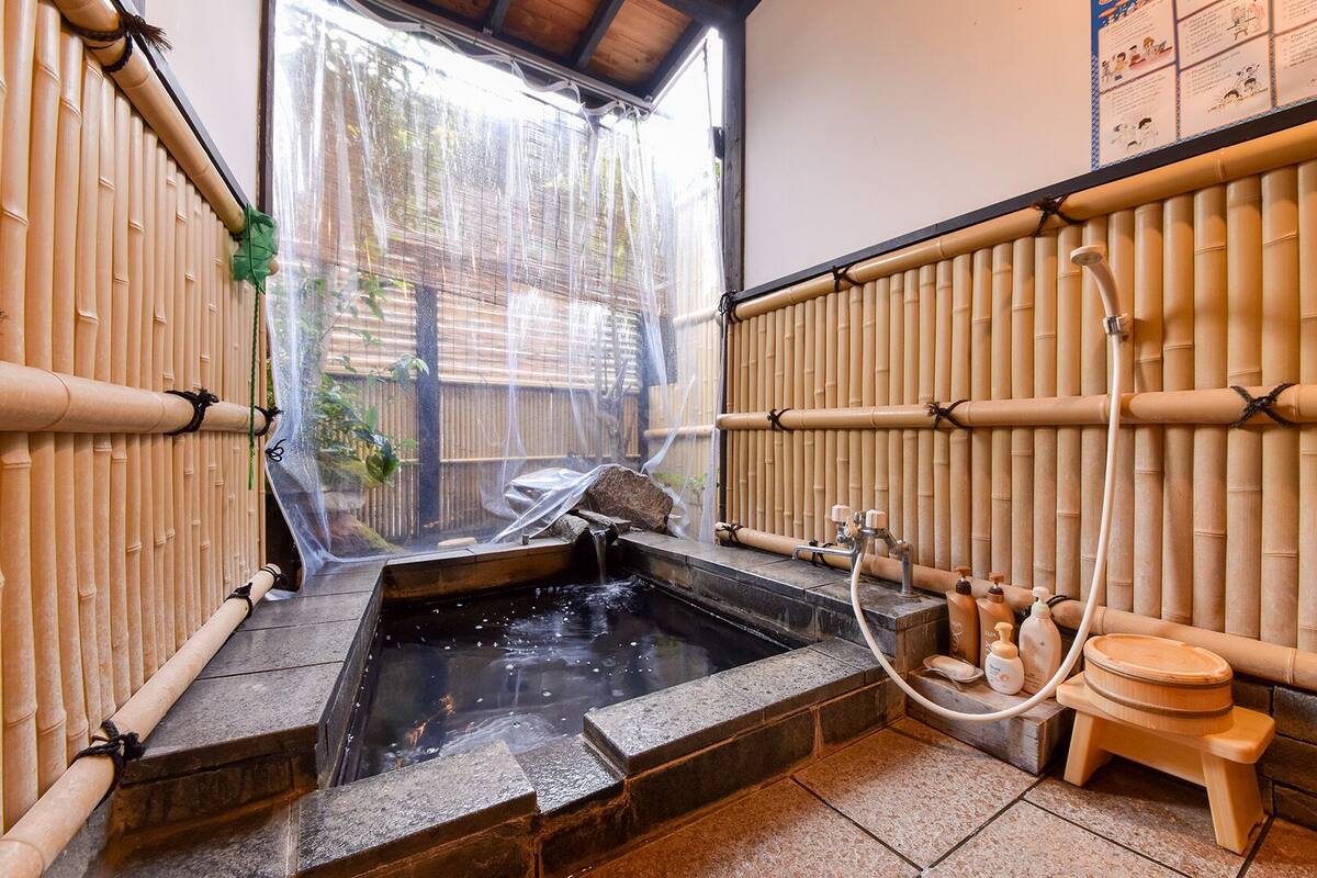 A traditional Japanese onsen with bamboo walls, a stone hot spring, and a wooden washbasin.