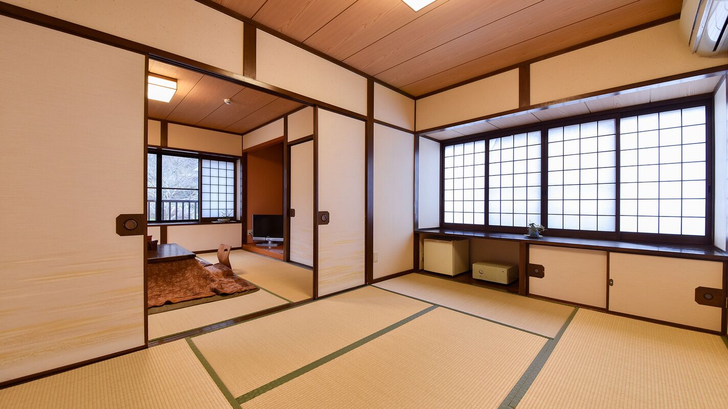 Ein traditioneller japanischer Raum mit Tatami-Boden, Schiebetüren, einem Fernseher und einem großen Fenster mit Gitterfenstern.