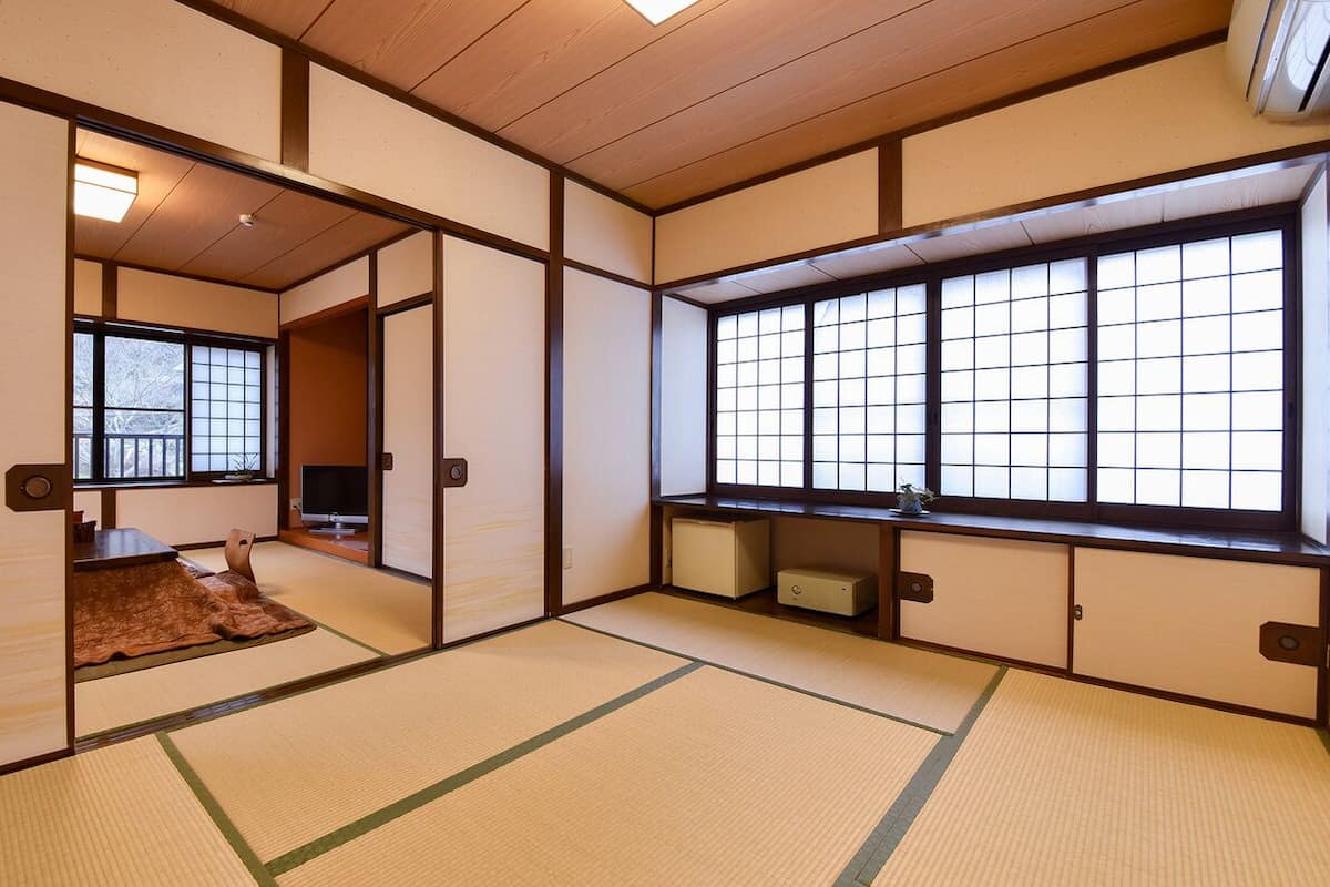 A traditional Japanese room with tatami flooring, sliding doors, a television, and a large window with grid panes.