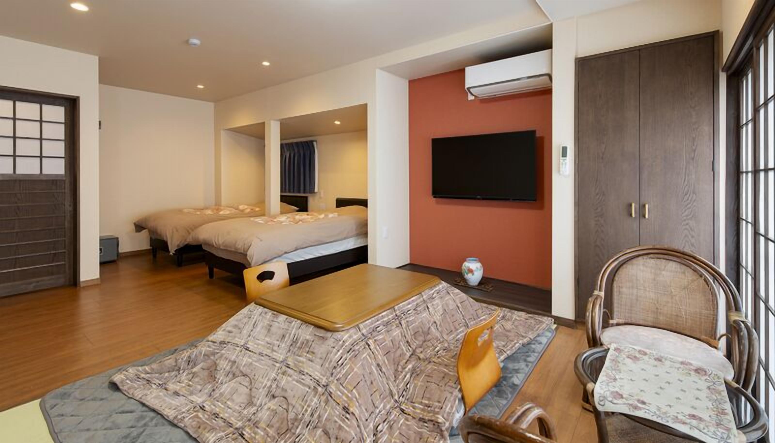 A room with two beds, a wooden table, a chair, a TV, and an air conditioning unit.