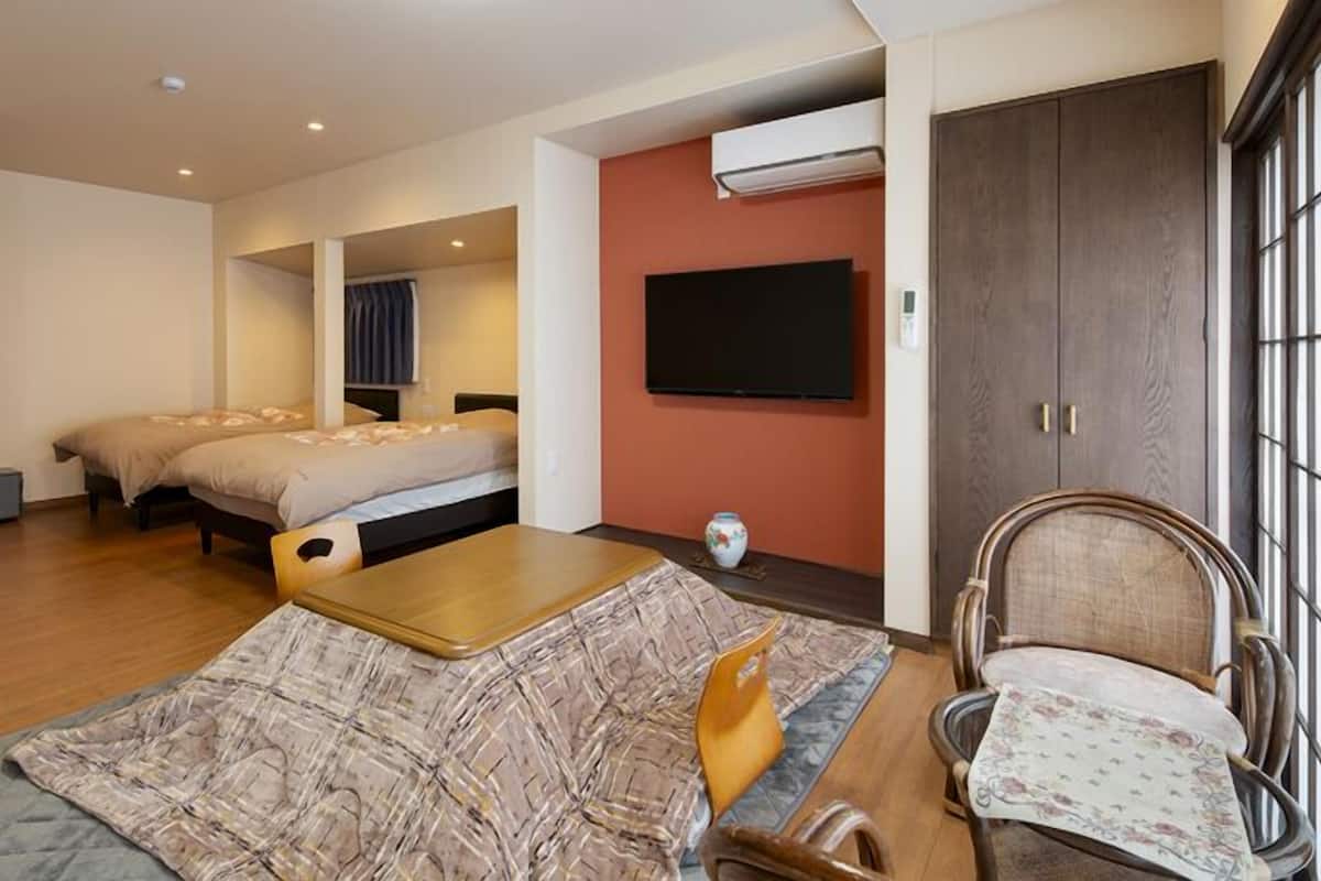 A room with two beds, a wooden table, a chair, a TV, and an air conditioning unit.