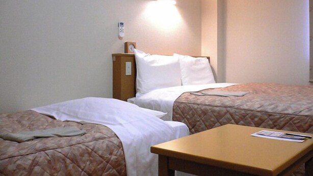 A hotel room with two beds, a small table, and a wall-mounted clock. - Hotel Joetsu Public City (Joetsu)