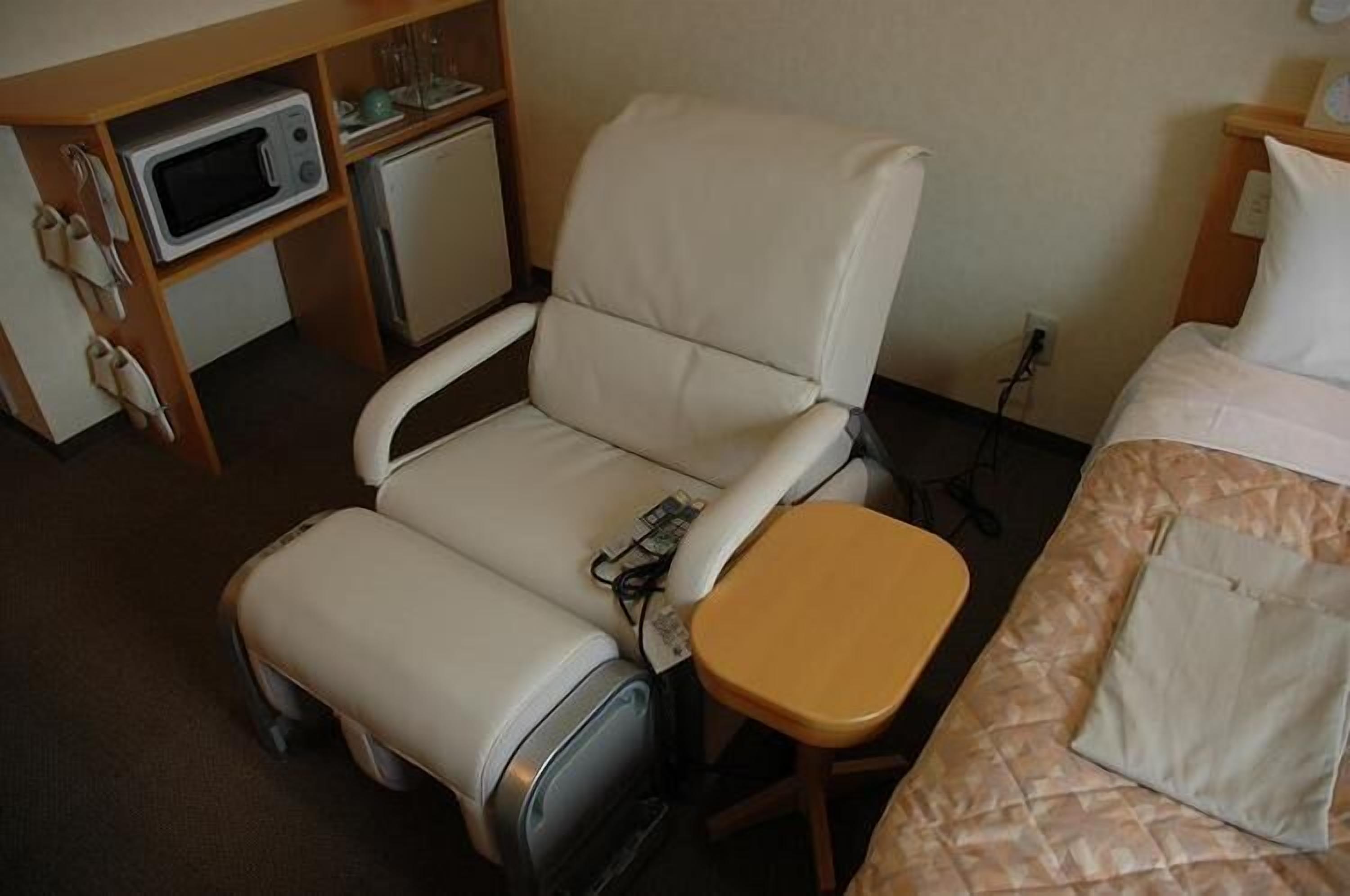 A hotel room with a single bed, a small desk with a microwave, a chair, and a small table.