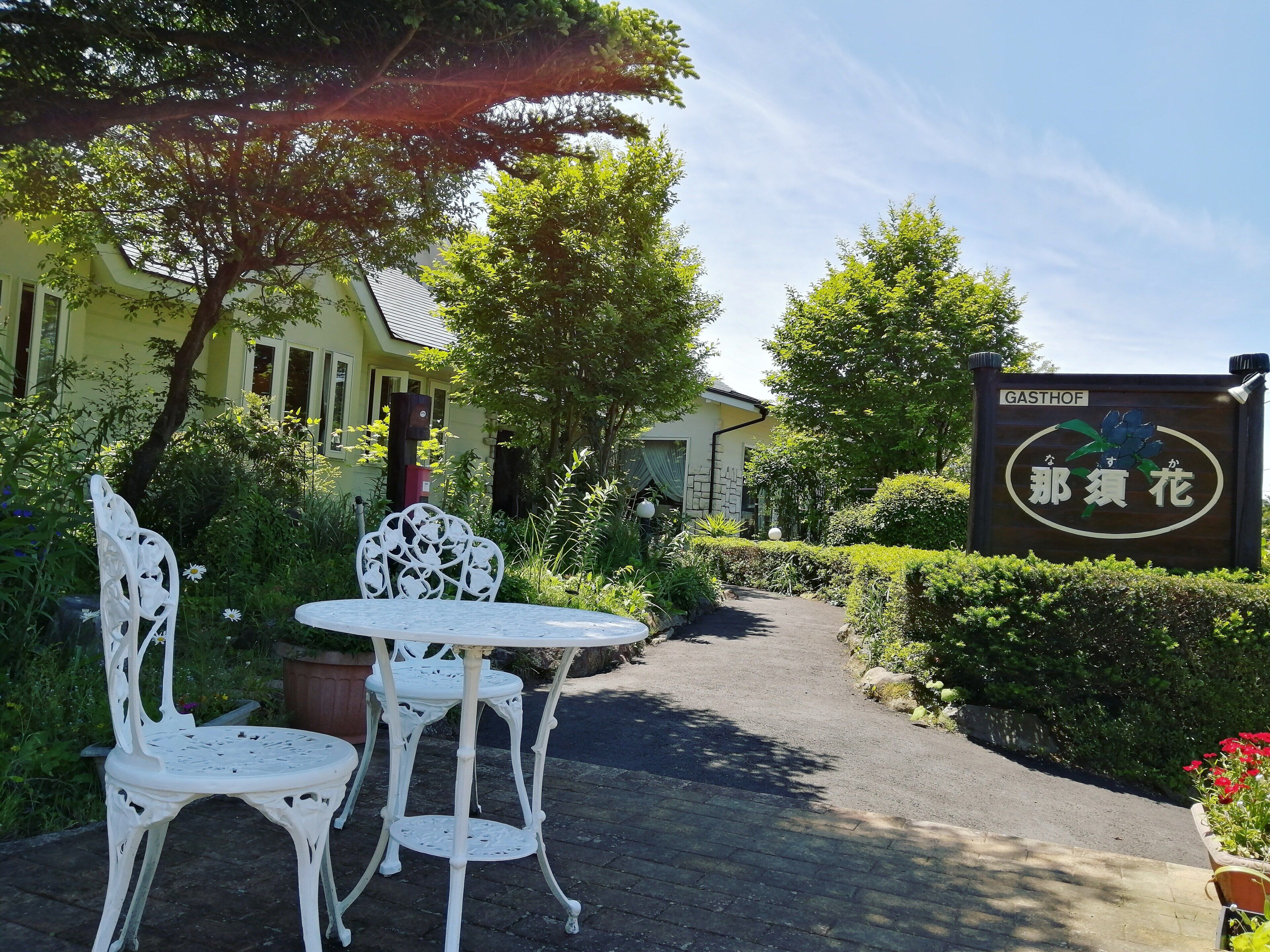 A garden area with white metal chairs and a table, a pathway leading to a building, and a sign with Chinese characters.