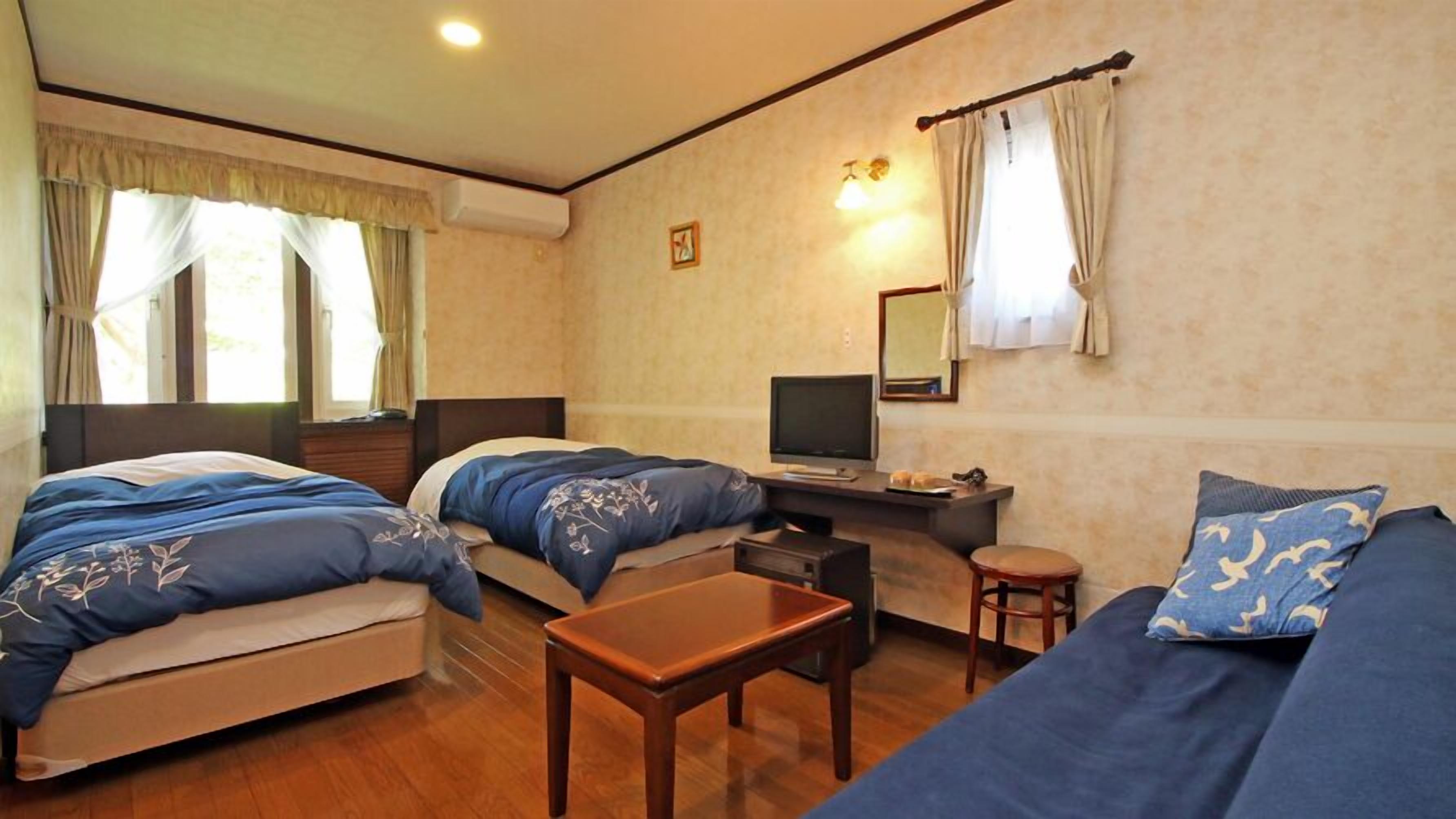 Una habitación con dos camas, un sofá, un televisor, una mesita y un espejo.
