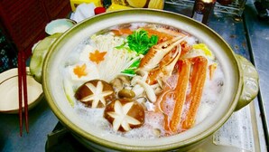 En gryta med soppa som innehåller olika ingredienser, till exempel svamp, tofu och bladgrönsaker.