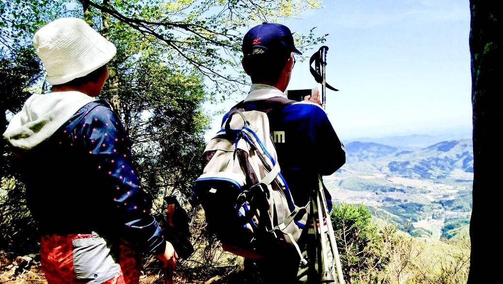 Two people hiking with backpacks, overlooking a mountainous landscape.