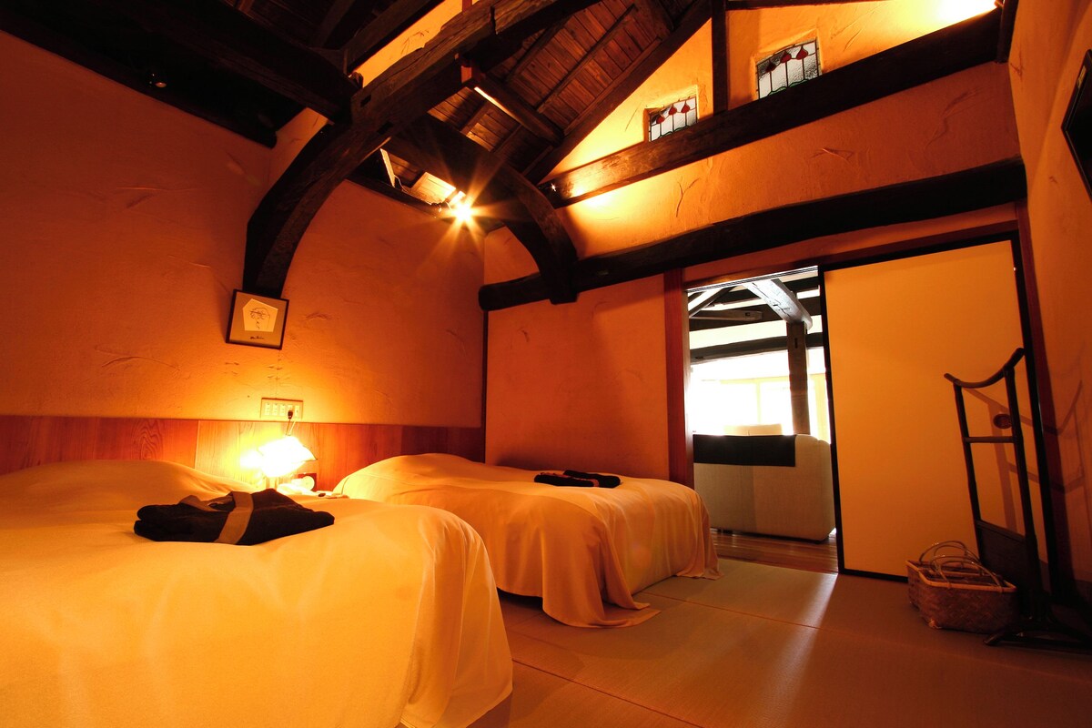 A hotel room with two beds, a wooden ceiling, and a small window.