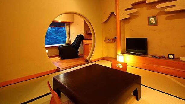 Una habitación con ventanal circular, televisión, mesa y una silla.