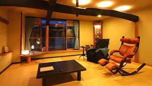 Una sala de estar con un sofá negro, un sillón mecedor, una mesita y una ventana con cortinas.